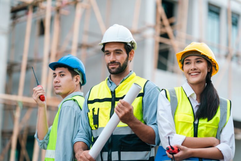 Construction worker team, hard hat, safety vest, engineering plan, smiling